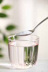 Spoon with baking soda over glass of water at white table against blurred background