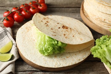 Tasty homemade tortillas, tomatoes, lime and lettuce on wooden table