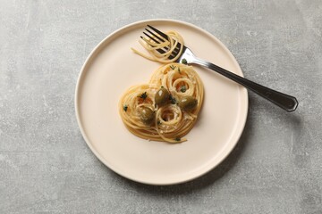 Heart made of tasty spaghetti, olives, cheese and fork on light grey table, top view