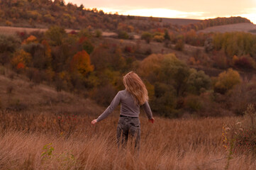 Young attractive blonde woman standing on the hill at sunset	