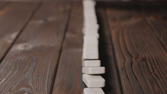 Close-up of a line of falling dominoes on a wooden surface. Domino Effect Concept. Concept of domino effect and chain reaction.