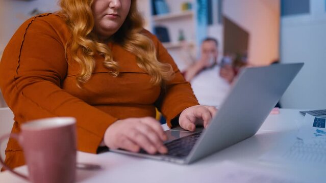 Plus size woman working on computer in office, drinking coffee, sedentary life