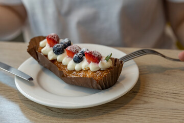 A close-up shot of a delicious pastry topped with fresh strawberries, blueberries, and whipped cream, resting on a white plate.