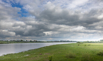 A picturesque view of a river flowing through a verdant landscape, with a canopy of white and gray clouds overhead.