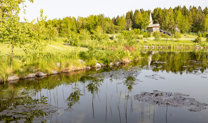 Obraz premium A peaceful pond in a lush forest, mirroring sky and trees. A quaint wooden building on the other side enhances the rustic beauty of this serene scenery.