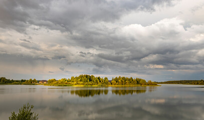 A picturesque view of a tranquil lake with a small island in the distance, surrounded by lush greenery and a sky adorned with fluffy clouds, creating a sense of serenity and peace.