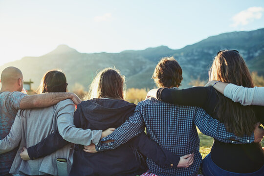 Friendship, sunset and group in nature with hug for adventure, travel or weekend trip in countryside. Rear view, outdoor and people with embrace for vacation, support or bonding together in Australia