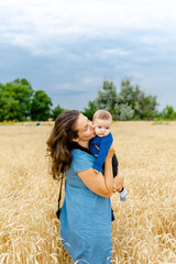 A young woman with her little son stands in a wheat field in the summer. Harmonious parenting of children.