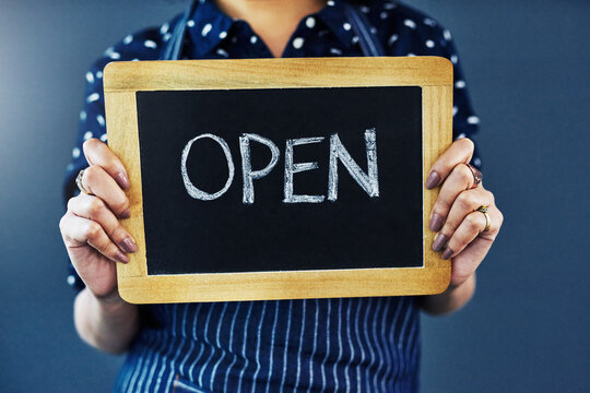 Woman, hands and chalkboard with open sign for welcome or introduction on a studio background. Closeup of female person or waitress with billboard or poster ready for service at cafe or restaurant