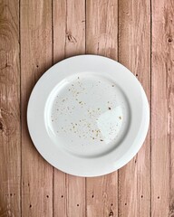 Bread, biscuit, or wafer crispy food crumbs on top of white plate. Finished eating dessert themed image. Object photography isolated on vertical ratio wooden surface background.