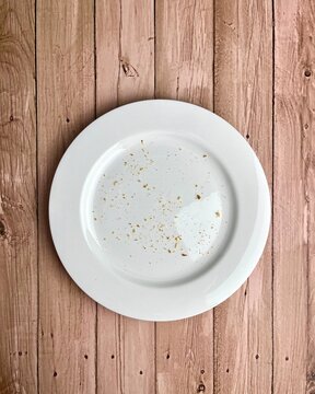 Bread, biscuit, or wafer crispy food crumbs on top of white plate. Finished eating dessert themed image. Object photography isolated on vertical ratio wooden surface background.