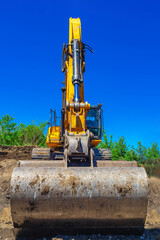 Front view of yellow excavator bucket against blue sky. Close. Excavator at the construction site.