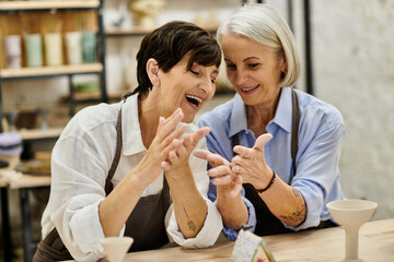 Two women are laughing together while crafting at a pottery studio.