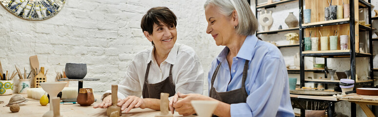 Two mature women work on pottery projects together in an art studio.