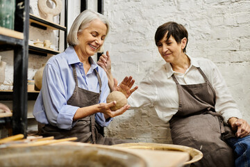 Two mature women craft pottery together in a cozy art studio.