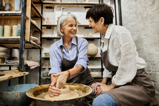 Two women work on a pottery wheel together in a studio. - Powered by Adobe