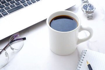 机にノートパソコンやノートを広げ、コーヒーを飲みながらデスクワークをしているイメージ
