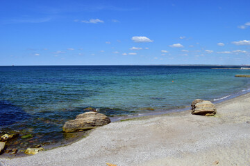 A picturesque seascape overlooking the blue sea, rocks and stones on a bright sunny day. The waves break against the rocks. the stone lies on the beach. coastline, leisure concept, tourism, vacation