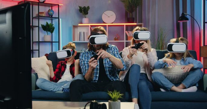 Happy family playing video games in augmented reality goggles and celebrating victory at home in the evening. Virtual entertainment concept
