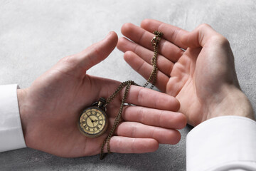 Fototapeta premium Man holding chain with elegant pocket watch at grey textured table, closeup