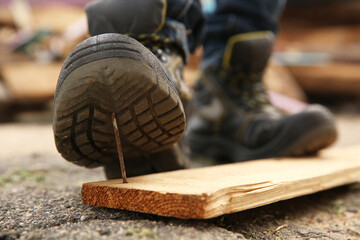Careless worker stepping on nail in wooden plank outdoors, closeup