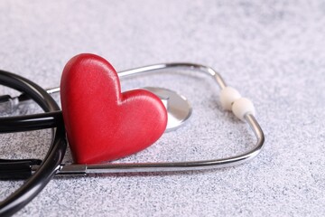 Stethoscope and red heart on grey stone table. Space for text