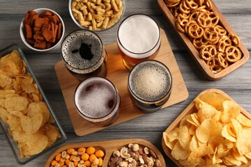 Glasses with different types of beer and snacks on grey wooden table, flat lay