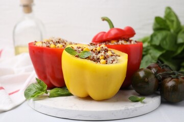 Quinoa stuffed bell peppers, basil and tomatoes on white table, closeup