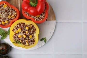 Quinoa stuffed bell peppers, tomatoes and basil on white tiled table, flat lay. Space for text