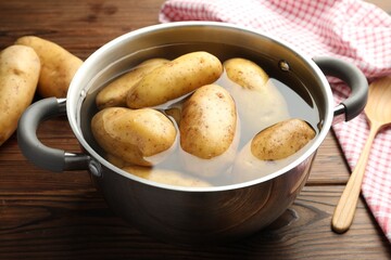 Raw potatoes in pot with water on wooden table