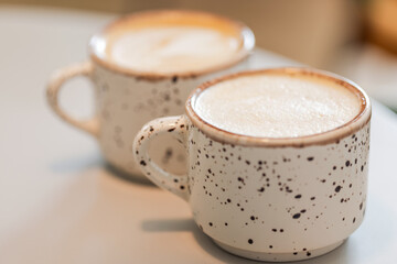 Two cups of cappuccino coffee stand on white table, close up photo
