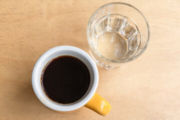 Yellow mug of black filter coffee and glass of water, top view