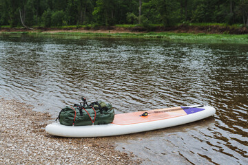 In a tranquil forest river setting, an inflatable paddleboard and gear invite you for a peaceful outdoor adventure in lush nature with calm waters and a serene ambiance