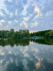 Fantastic cloudy sky reflection on the lake surface, trees silhouettes reflection on the lake, evening twilights lake in the park