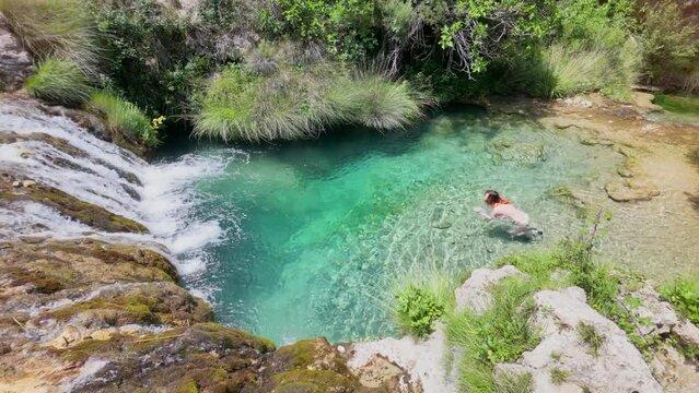 A woman is swimming in a small body of water. The water is clear and the surrounding area is lush and green