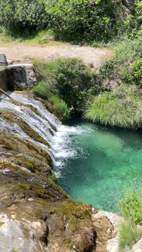 A waterfall with a greenish-brown color. The water is flowing down the rocks. The rocks are covered with moss