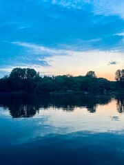 Fototapeta premium Fantastic cloudy sky reflection on the lake surface, trees silhouettes reflection on the lake, evening twilights lake in the park