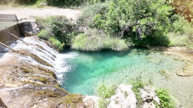 A waterfall is flowing into a small pool of water. The water is clear and calm. The scene is peaceful and serene