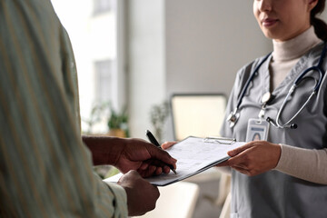 Close up of unrecognizable man signing medical form on clipboard in clinic copy space