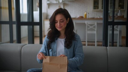 Caucasian hunger girl female unpacking open paper bag take away order meal at couch sofa woman at home sniff delivery package good smell aroma tasty fast food dish cafe restaurant courier service