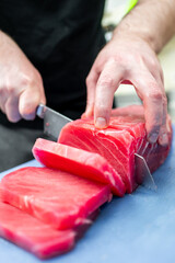 Close-up of hands precisely slicing fresh red tuna on a blue cutting board, highlighting the art of food preparation