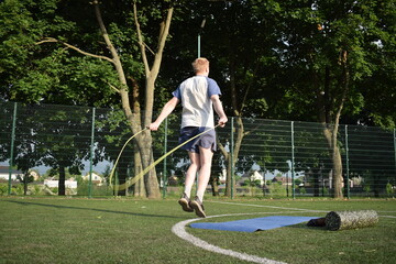 Obraz premium A young man in sportswear engages in a workout, using a sport tool for physical exercises on a sports field in the morning. His dedication to fitness performs training routine with focus and energy