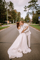 Valmiera, Latvia - September 9, 2023 - Bride and groom kissing in the middle of a road, surrounded by trees and street signs, with the bride in a flowing white dress and groom in a light suit.