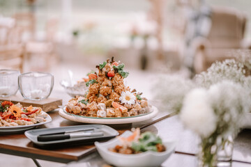 Valmiera, Latvia - September 9, 2023 - Plated dish with a decorative pile of breaded chicken and garnish, surrounded by floral arrangements and elegant table setting.