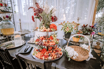 Valmiera, Latvia - September 9, 2023 - An elegant table setup with a tiered fruit platter, decorative plants, a wicker basket with flowers, and a beverage dispenser.