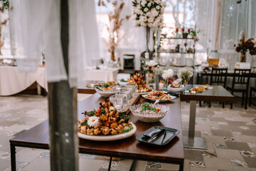 Valmiera, Latvia - September 9, 2023 - A buffet table set with various dishes and glassware in an elegantly decorated room with floral arrangements and soft natural light.