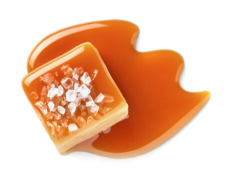 One salted or salty caramel candy cube topped with caramel sauce and salt on white background.