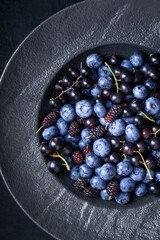 Top view of fresh blueberries, blackcurrant berries and mulberries in a black plate. Food photography