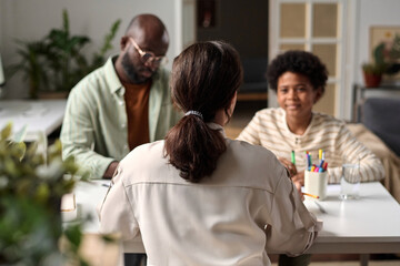 Back view of female social worker or psychologist consulting African American family of father and son sitting at table in office, copy space