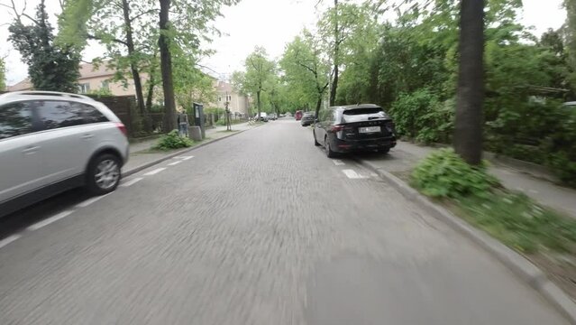 This is a video of a residential street with cars parked on both sides. The street is lined with trees and there are houses on either side. The video is taken from the perspective of a driver driving
